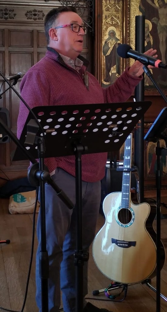 Gareth in Cranberry-coloured Weird Fish top and blue Chinos teaching a song.